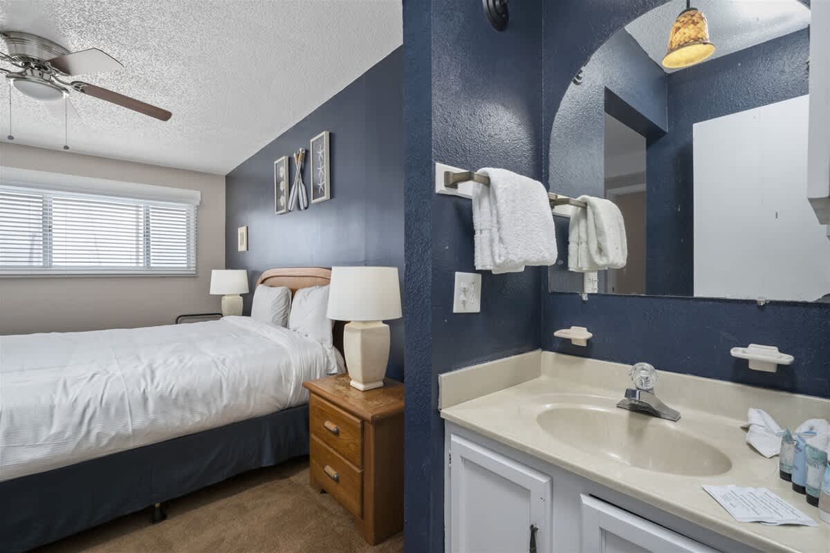 The Summit 613 – Compact bedroom with a queen bed, en-suite bathroom, and blue accent walls.