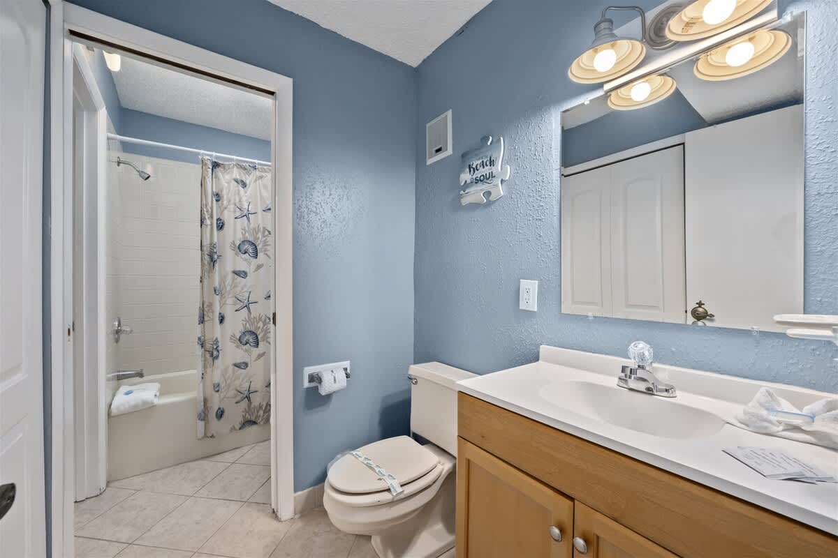 The Summit 613 – Bathroom with blue walls, shower tub combo, wooden vanity, and lighted mirror.