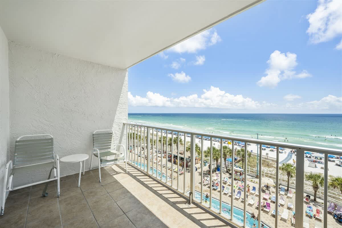 The Summit 613 – Balcony view from The Summit 613 overlooking the beach, ocean, and pool area with patio chairs.