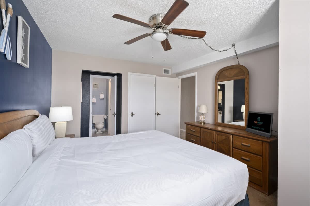 The Summit 613 – Bedroom with a king bed, dresser, mirror, and ceiling fan; bathroom door visible.