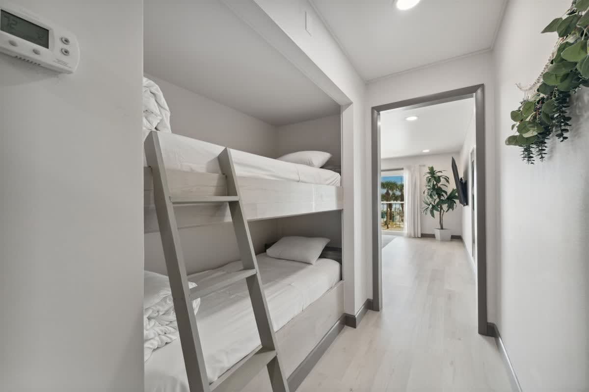 The Summit 215 – Bunk beds in a hallway leading to a bright room with a view of palm trees.