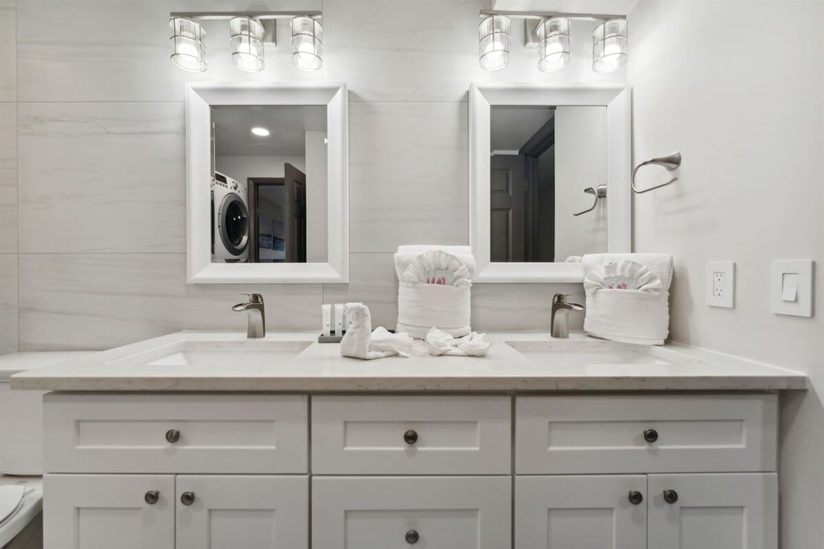 The Summit 215 – Modern bathroom with double sinks, mirrors, and stacked washer-dryer unit. White cabinetry and marble countertops.