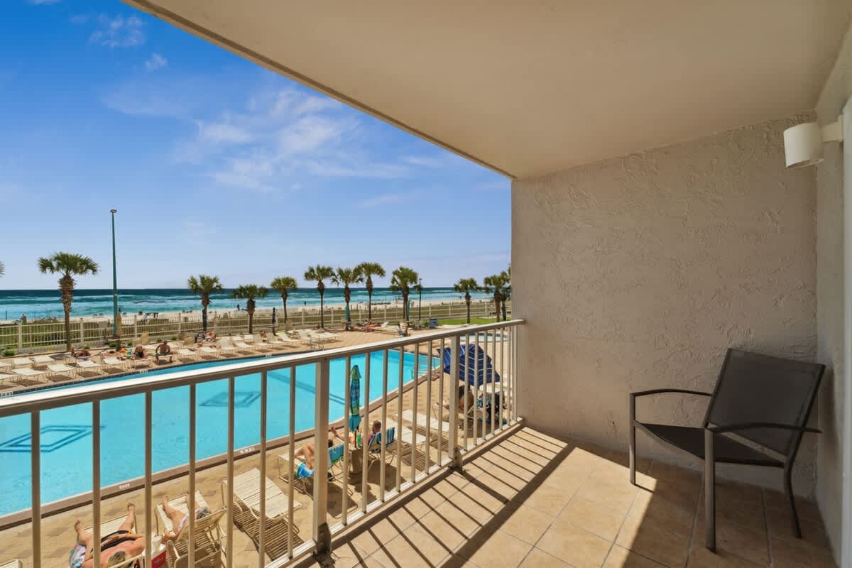 The Summit 215 – Balcony view of a pool and beach, featuring palm trees and lounge chairs.