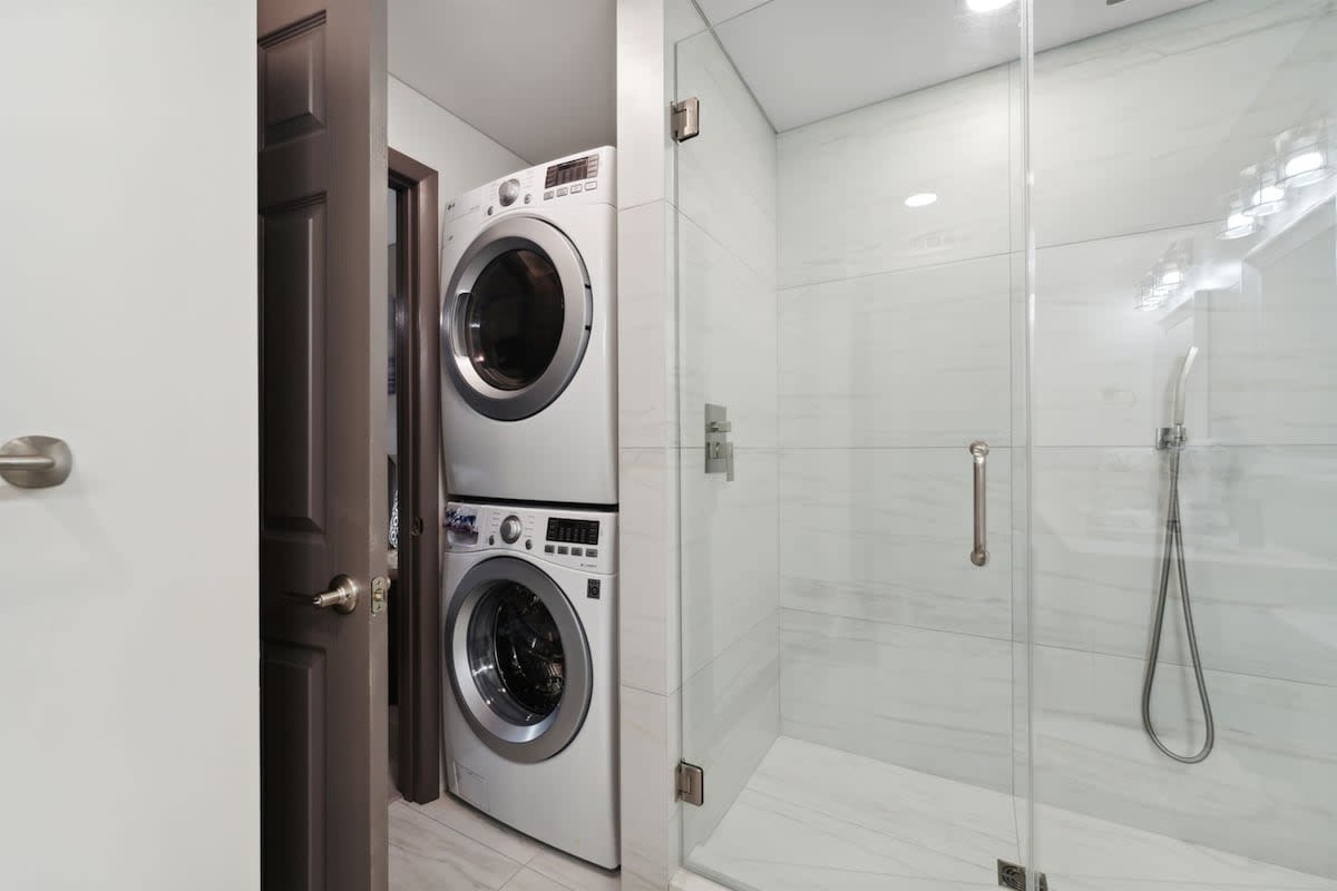 The Summit 215 – Laundry machines stacked next to a glass-enclosed shower in a modern bathroom.