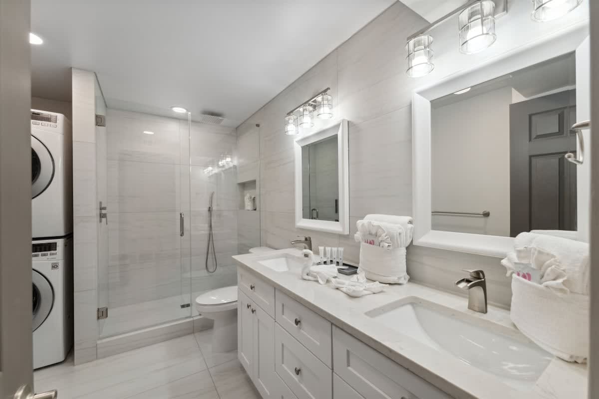 The Summit 215 – Modern bathroom with double sinks, glass shower, laundry machines, and contemporary lighting.