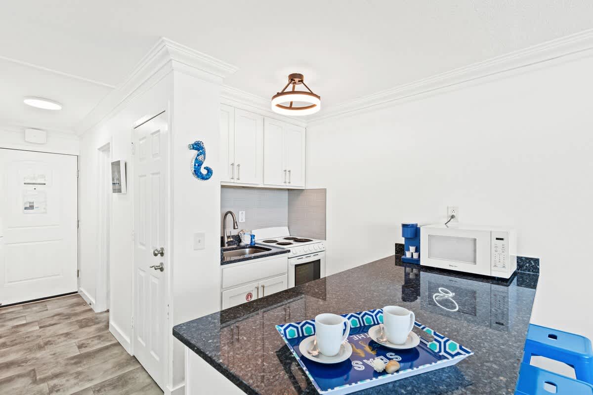 Top Of The Gulf 607 – Kitchen area with granite countertops, white cabinets, coffee maker, and two cups on a tray.