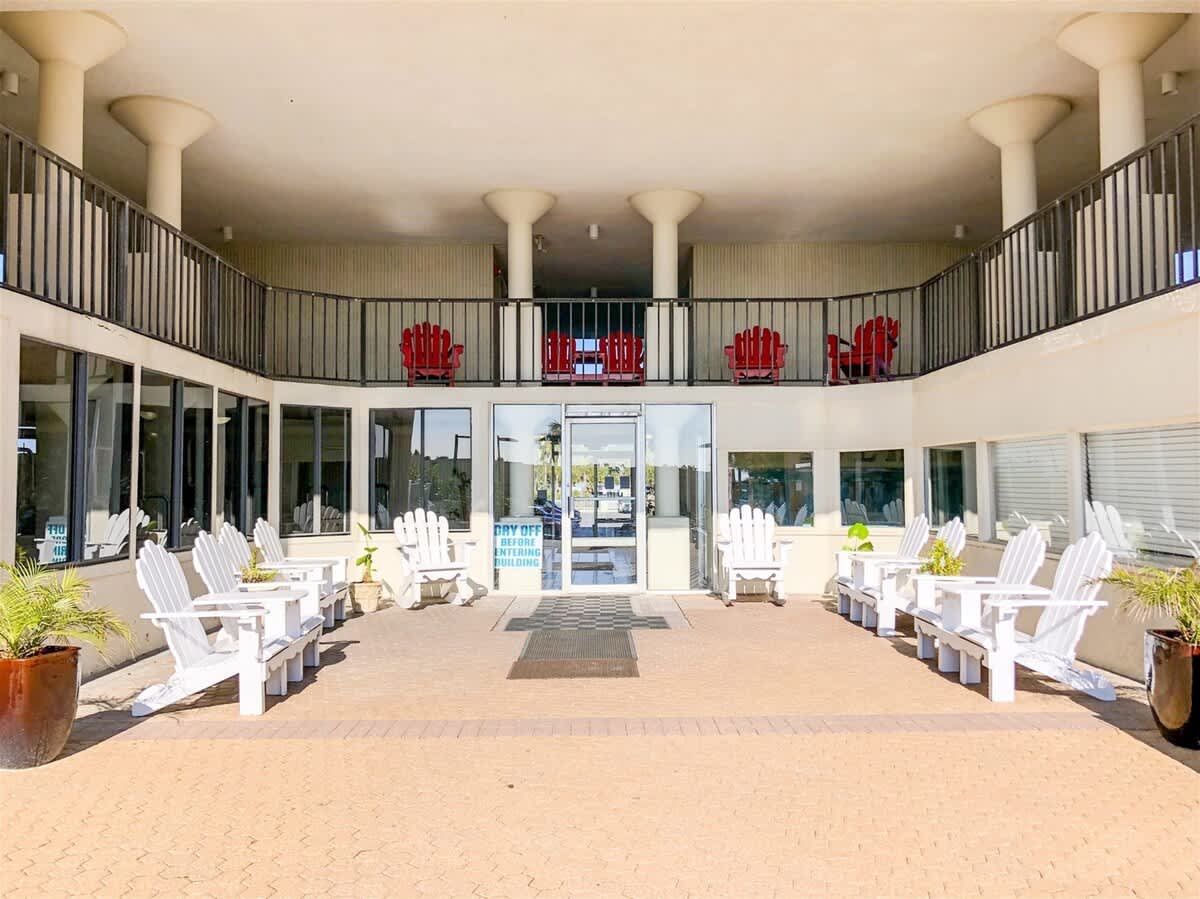 Top Of The Gulf 607 – Entrance area with white Adirondack chairs, glass doors, and red chairs on the balcony above.