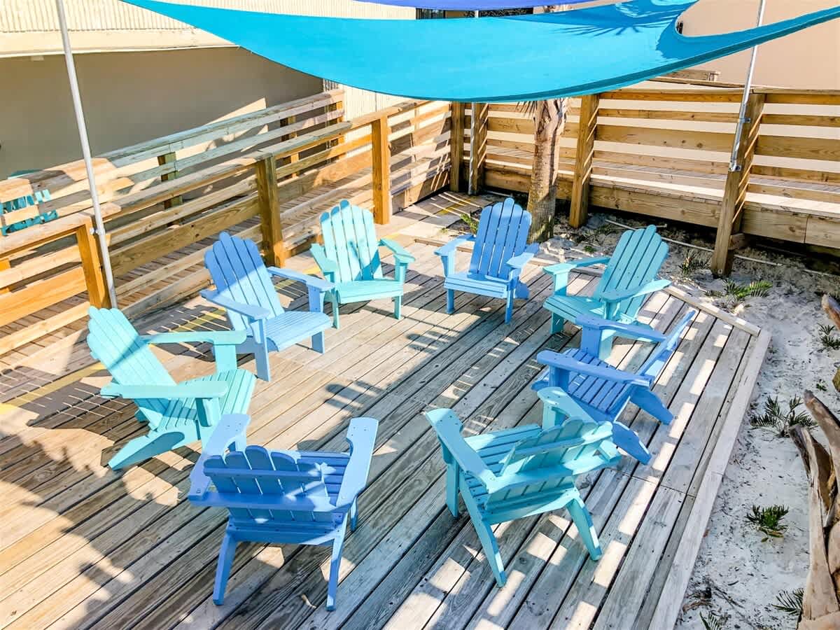 Top Of The Gulf 607 – Outdoor deck with blue adirondack chairs arranged in a circle under a shade sail.