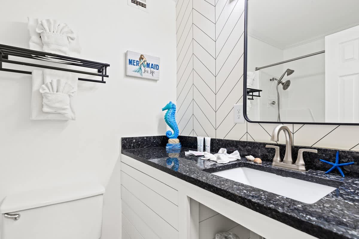 Top Of The Gulf 607 – Bathroom with black granite countertop, sink, mirror, shower, and decorative sea-themed accents.