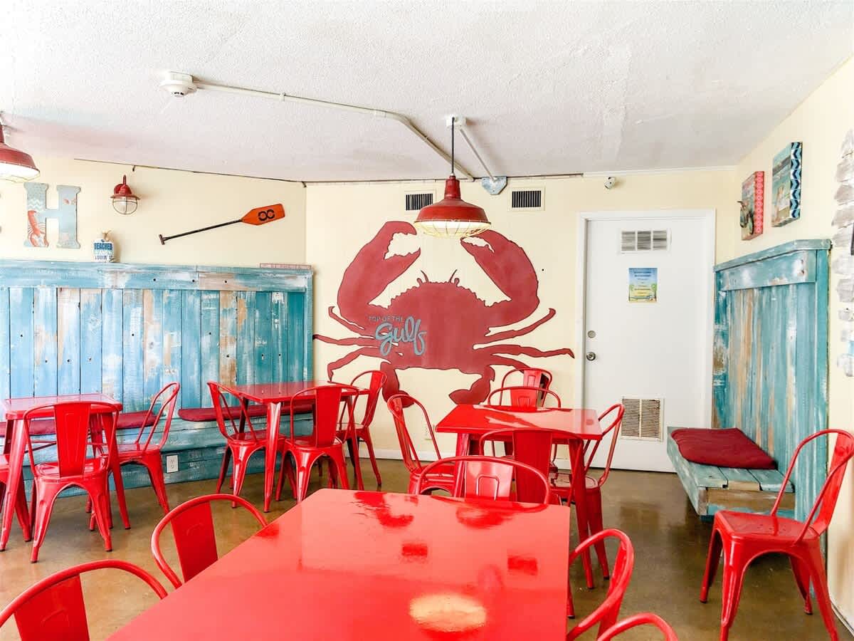 Top Of The Gulf 607 – Brightly colored dining area with red tables and chairs, featuring a large crab mural on the wall.