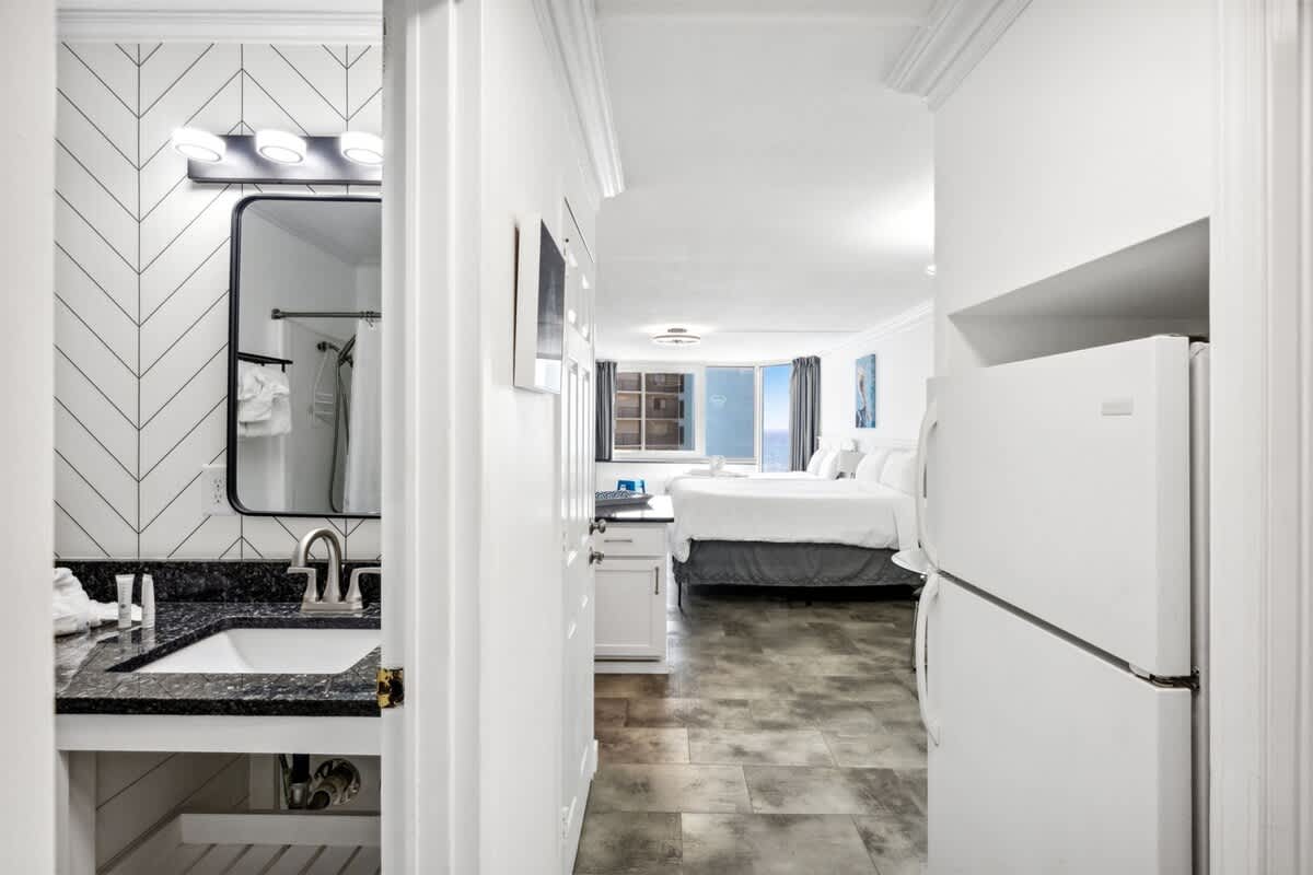 Top Of The Gulf 607 – Interior view of a vacation rental featuring a kitchenette, bathroom, and bedroom with two beds and ocean view.