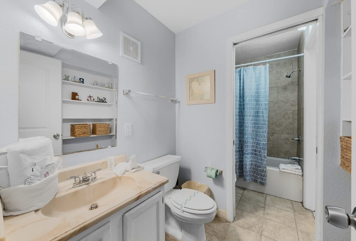 The Summit 606 – Small bathroom with a sink, toilet, and bathtub with a blue shower curtain.