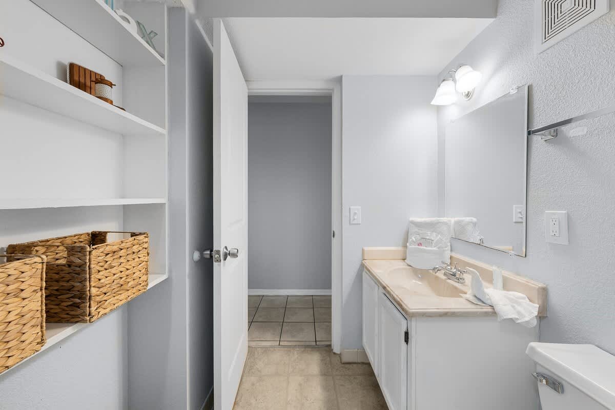 The Summit 606 – Bathroom with a double sink vanity, shelves, and a door leading to another room.