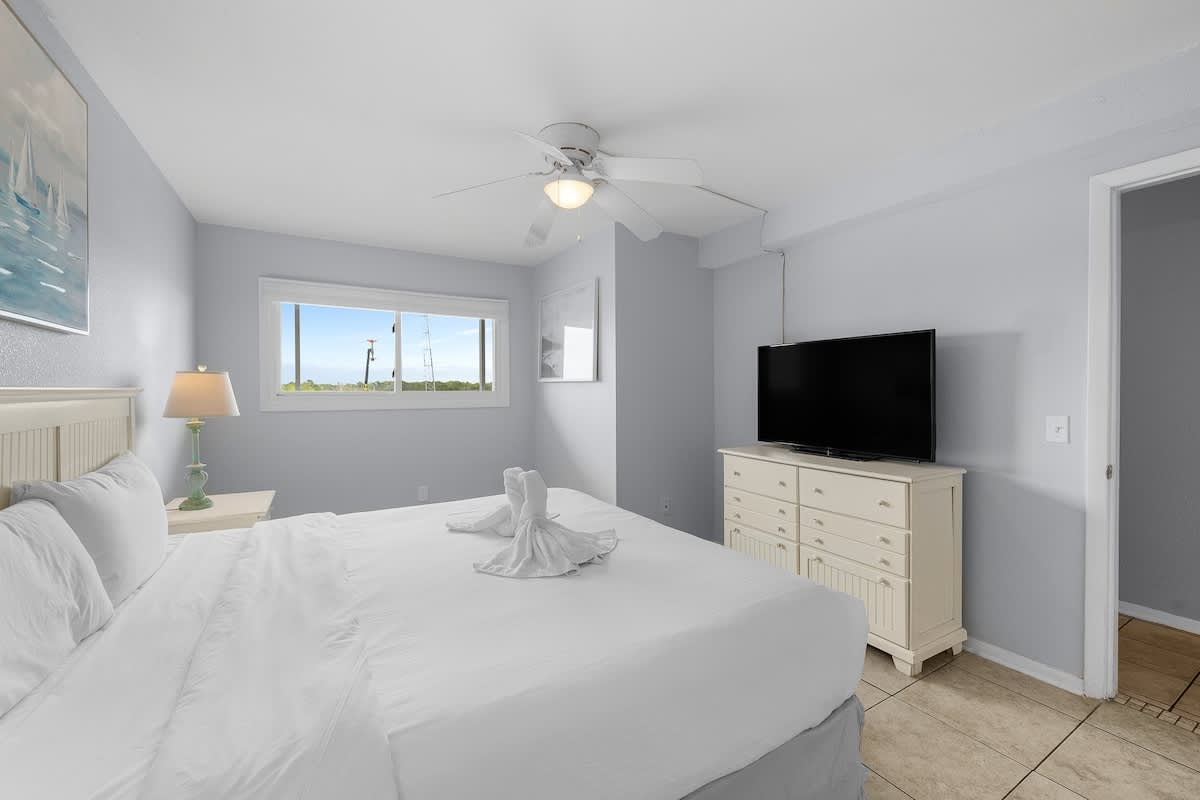 The Summit 606 – Light blue bedroom with a queen bed, dresser, TV, and window view of outdoors.
