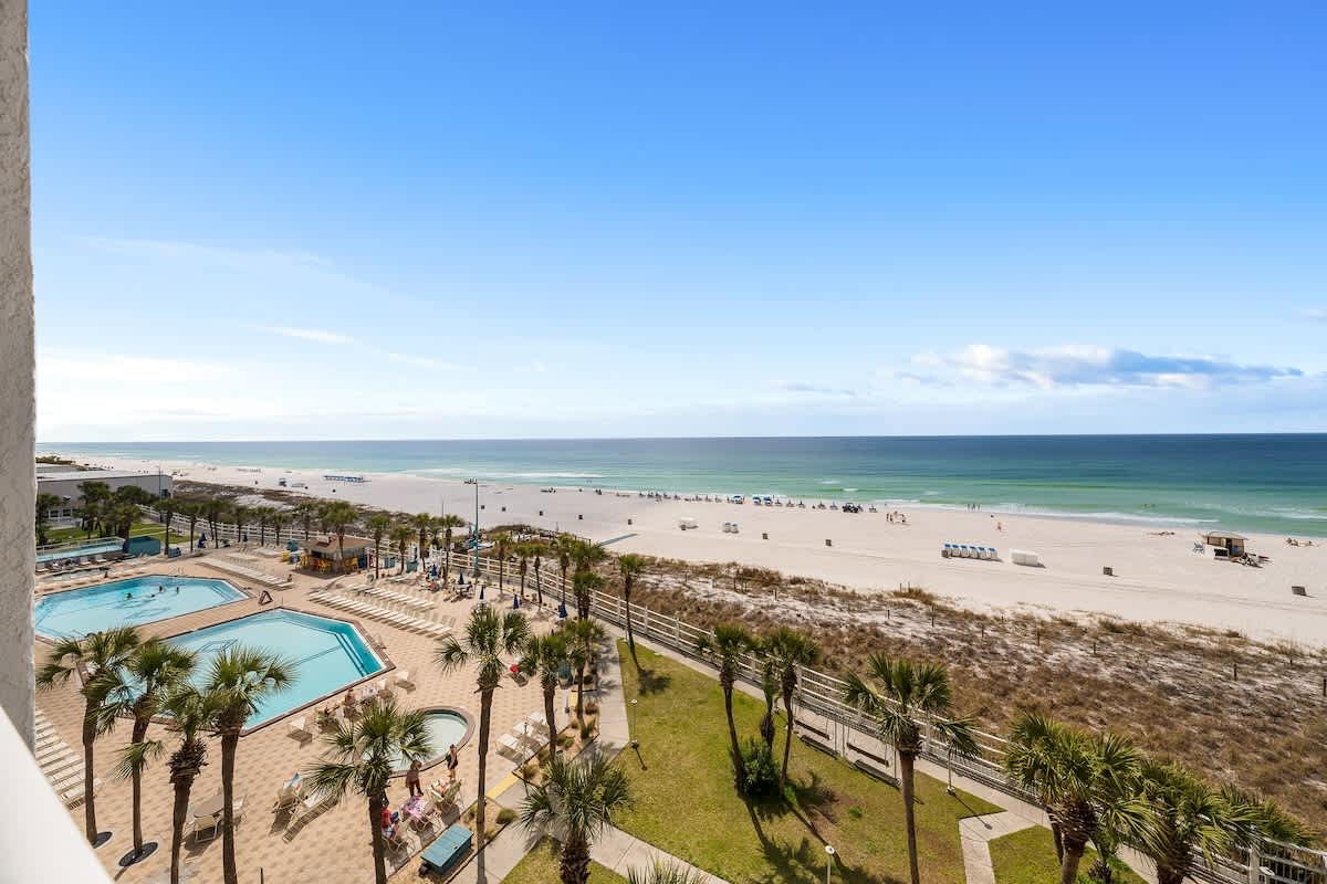 The Summit 606 – Beachfront view from a balcony showing a pool area, palm trees, and a sandy beach.