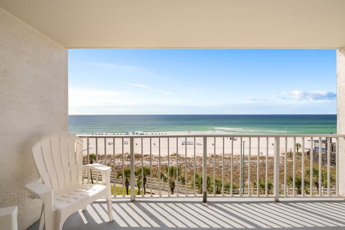The Summit 606 – Balcony view overlooking the beach with a white Adirondack chair and ocean in the background.