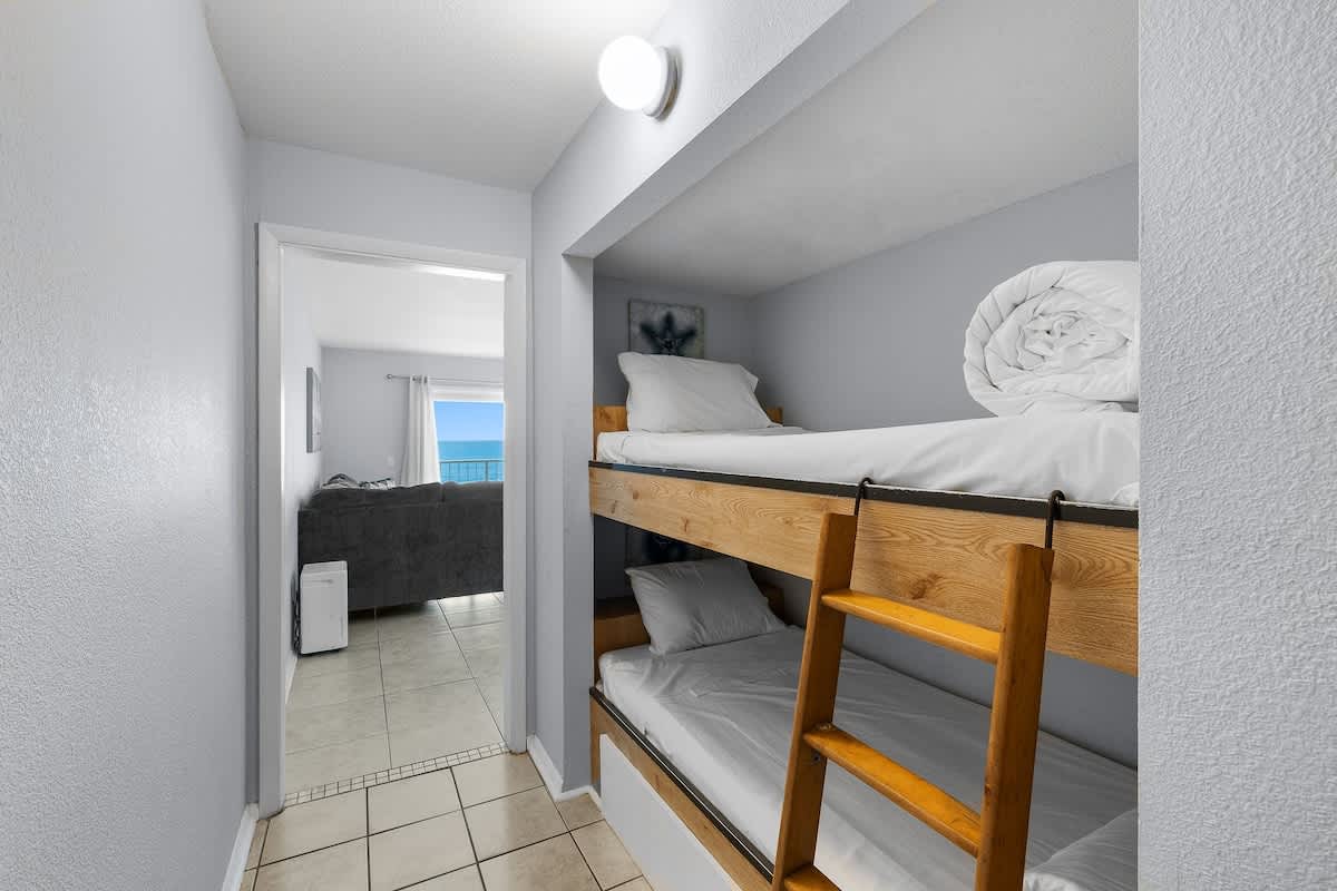 The Summit 606 – Bunk beds in a hallway, with a view of ocean and living area visible through doorway.