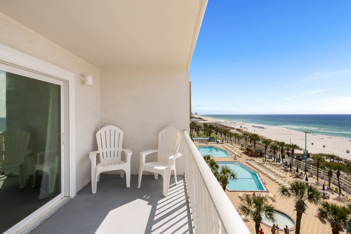 The Summit 606 – Balcony with two white chairs overlooking beach and swimming pools.