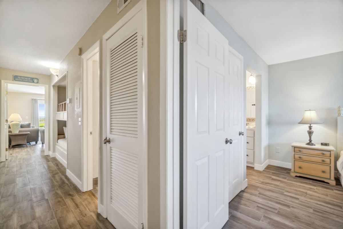 The Summit 108 – Hallway view with closed doors, light wood flooring, and a soft lamp beside a nightstand.
