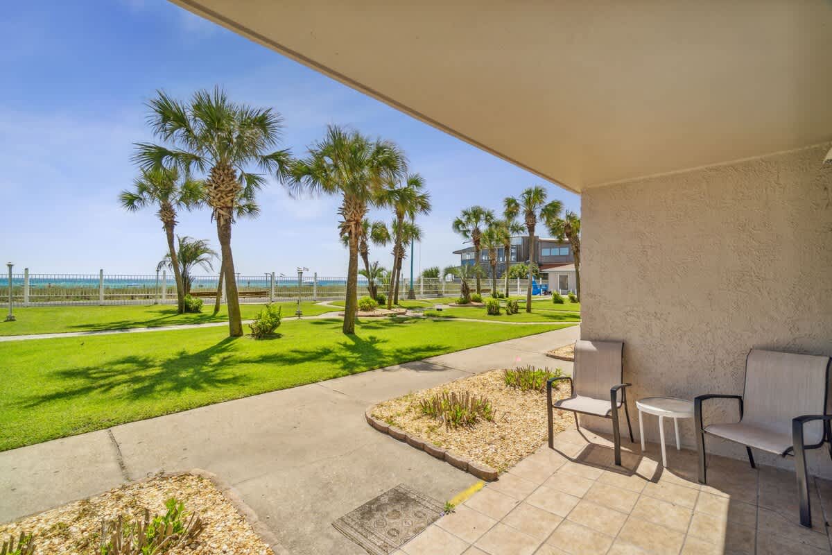 The Summit 108 – Patio view with two chairs, palm trees, and lawn leading to a beachfront.