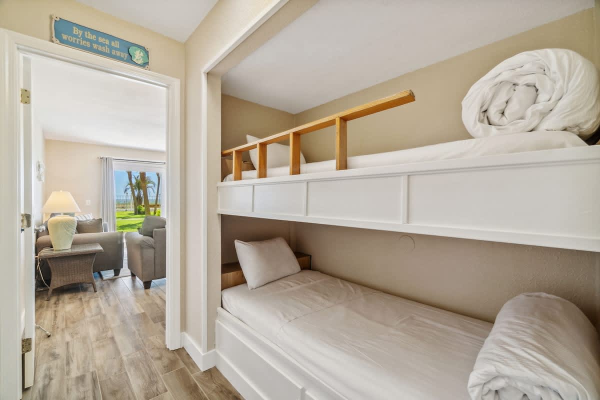 The Summit 108 – Bunk beds in a coastal vacation rental, with a view of palm trees through an adjacent living room.