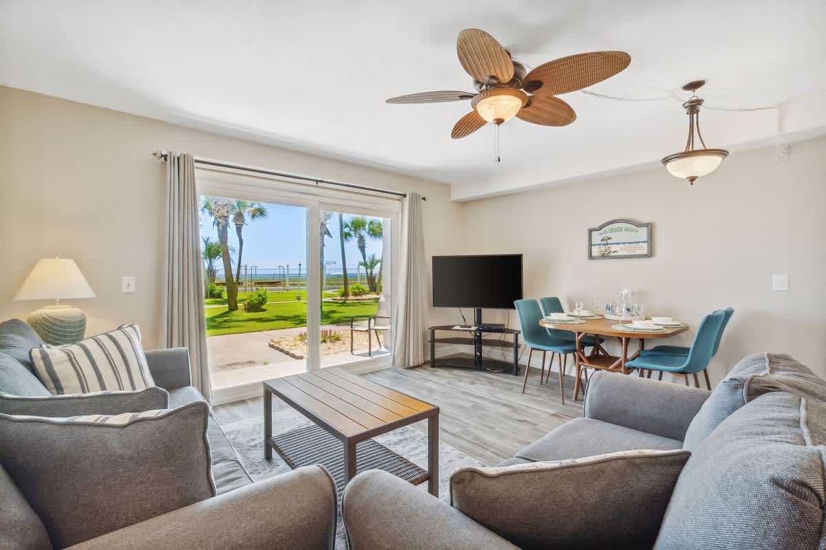 The Summit 108 – Living room with two sofas, dining area, TV, and sliding glass doors revealing lawn view.