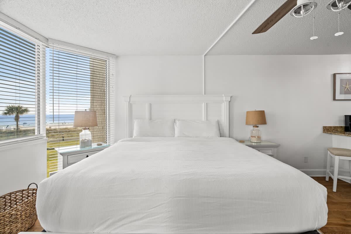 Top Of The Gulf 213 – Bright bedroom with a large bed, windows showing ocean view, and light-colored furniture.