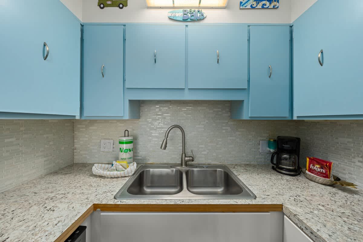 The Summit 1023 – Light blue cabinets above a double sink, granite countertop, coffee maker, and decorative items.