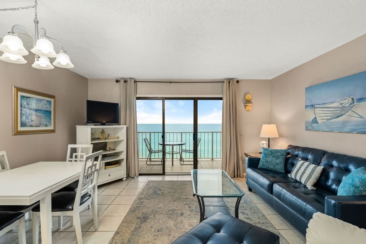 The Summit 1023 – Cozy living room with ocean view, blue sofa, dining table, and balcony access.