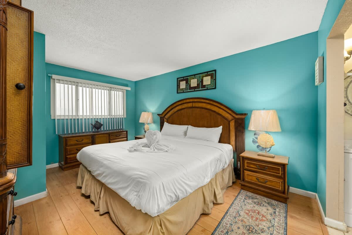 The Summit 1023 – Bedroom with a large bed, wooden furniture, blue walls, and natural light from a window.