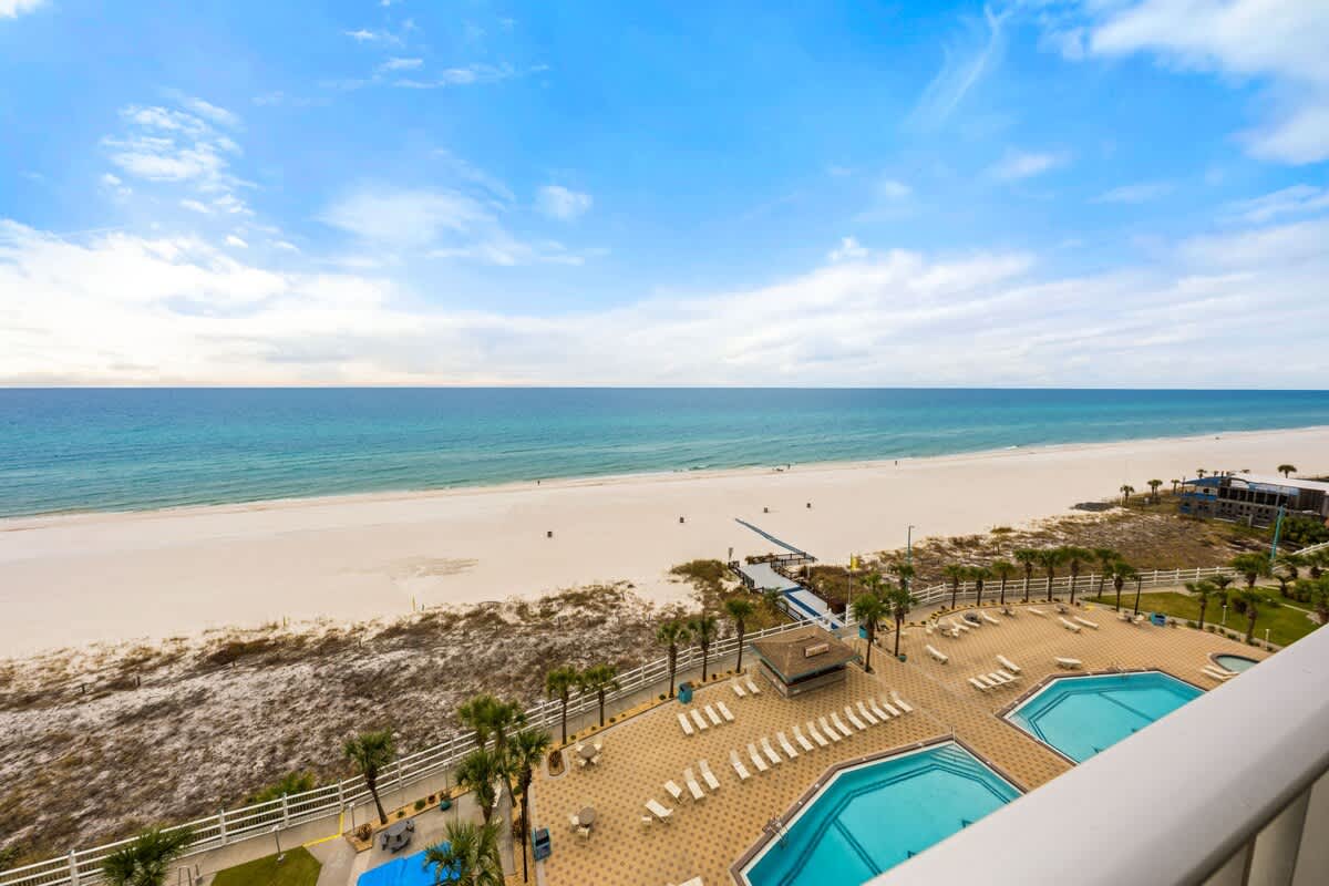 The Summit 1023 – View from balcony overlooking beach, two swimming pools, and palm trees.