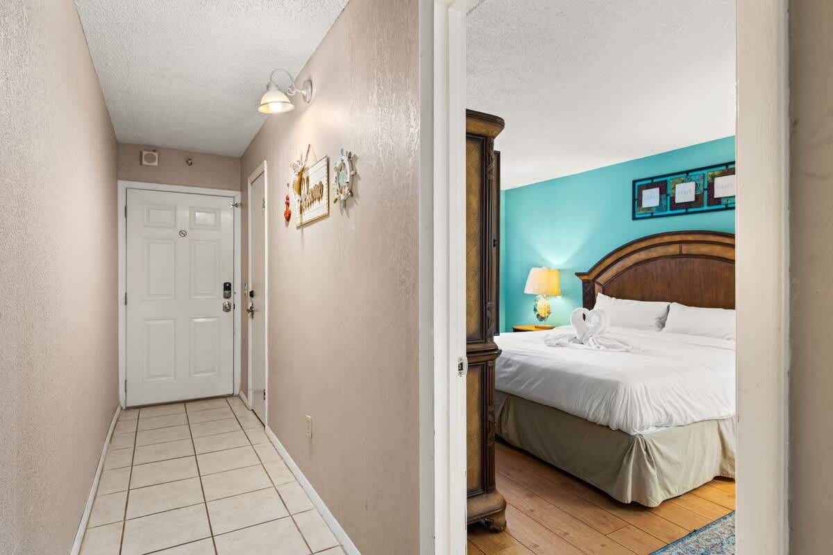 The Summit 1023 – Hallway leading to a teal bedroom with a queen bed and decorative towels.