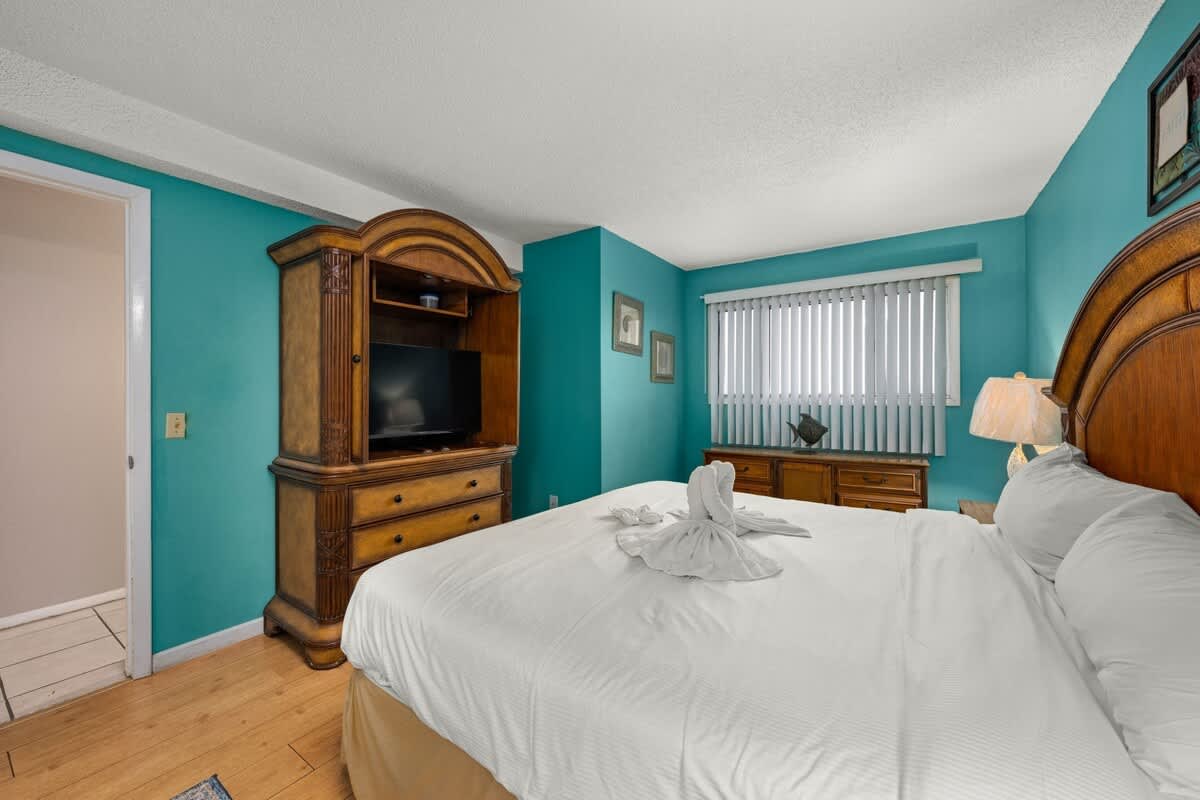 The Summit 1023 – Cozy bedroom with teal walls, wooden furniture, a TV, and a towel display on the bed.