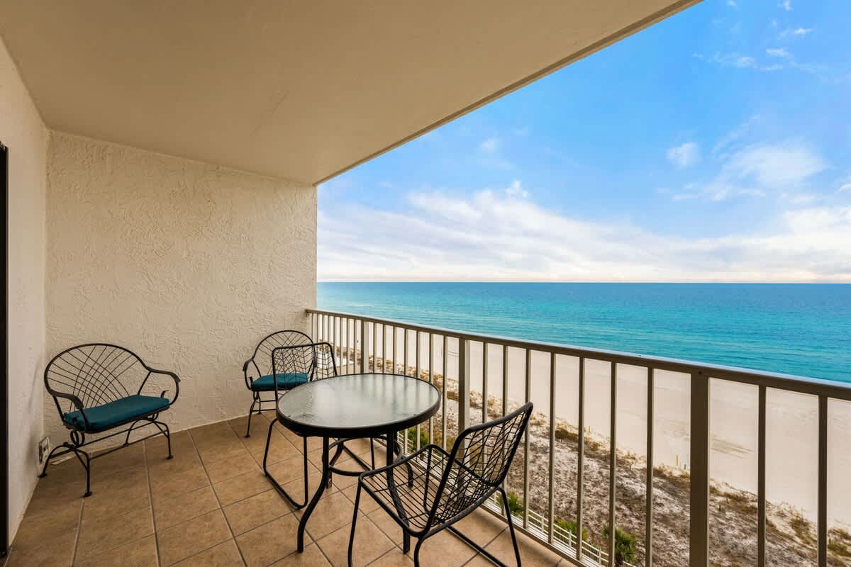 The Summit 1023 – Balcony with four metal chairs and a table, overlooking a sandy beach and ocean view.