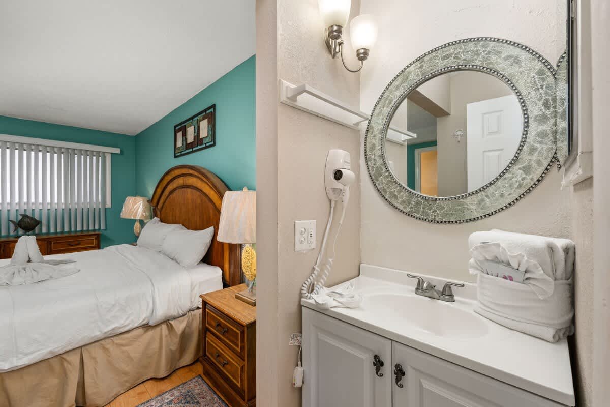 The Summit 1023 – Bedroom with a queen bed, decorative walls, and an adjoining bathroom with a sink and mirror.