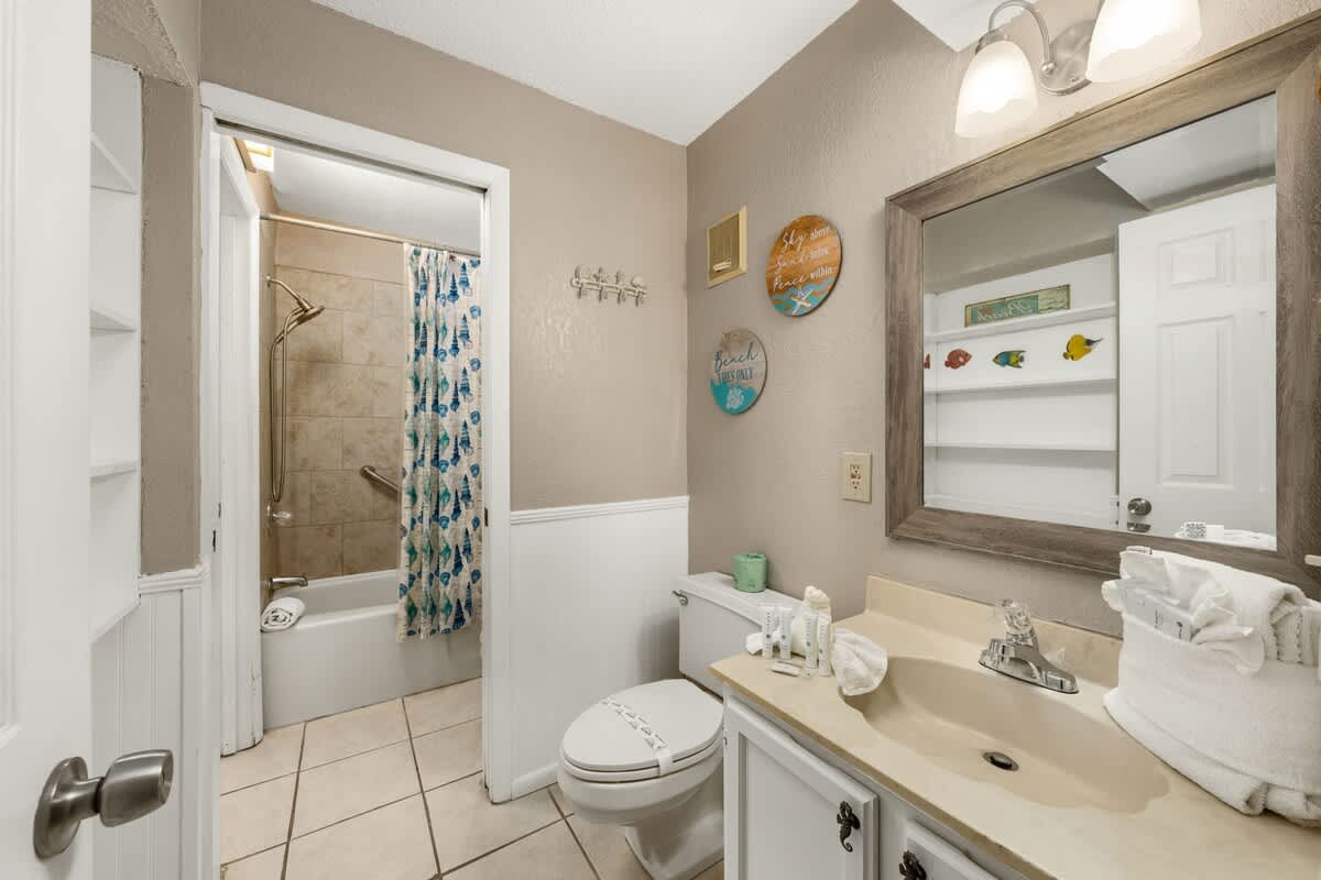 The Summit 1023 – Bathroom featuring a bathtub with shower, beige tiles, and decorative beach-themed wall art.