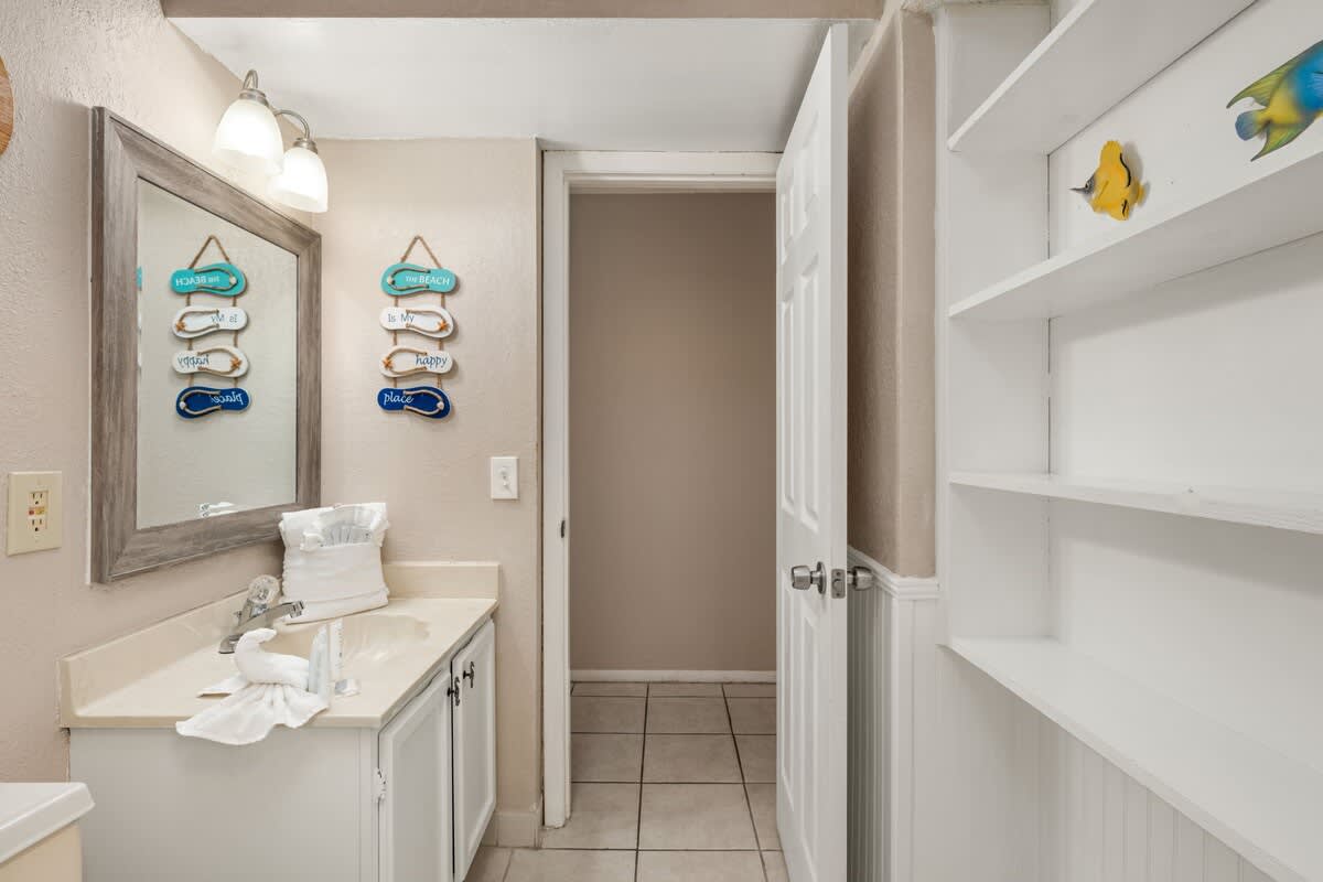 The Summit 1023 – Bathroom with a sink, mirror, decorative wall signs, and open shelving.