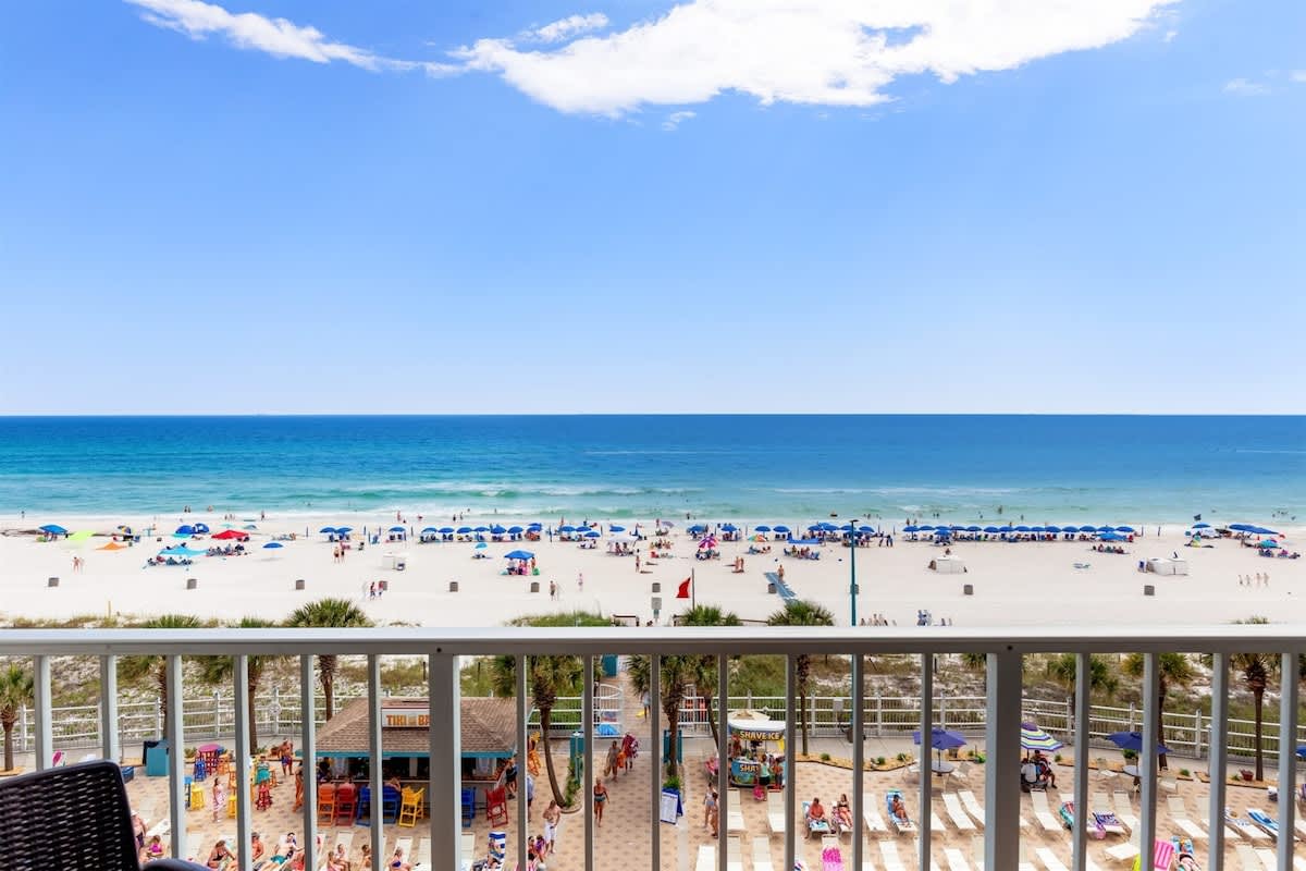 The Summit 616 – Balcony view of beach with umbrellas, clear blue water, and a beachfront bar area below.