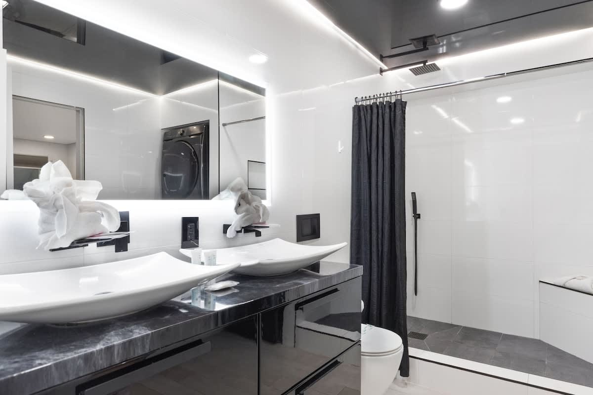 The Summit 616 – Modern bathroom featuring dual sinks, black cabinetry, a glass shower, and gray tiles.