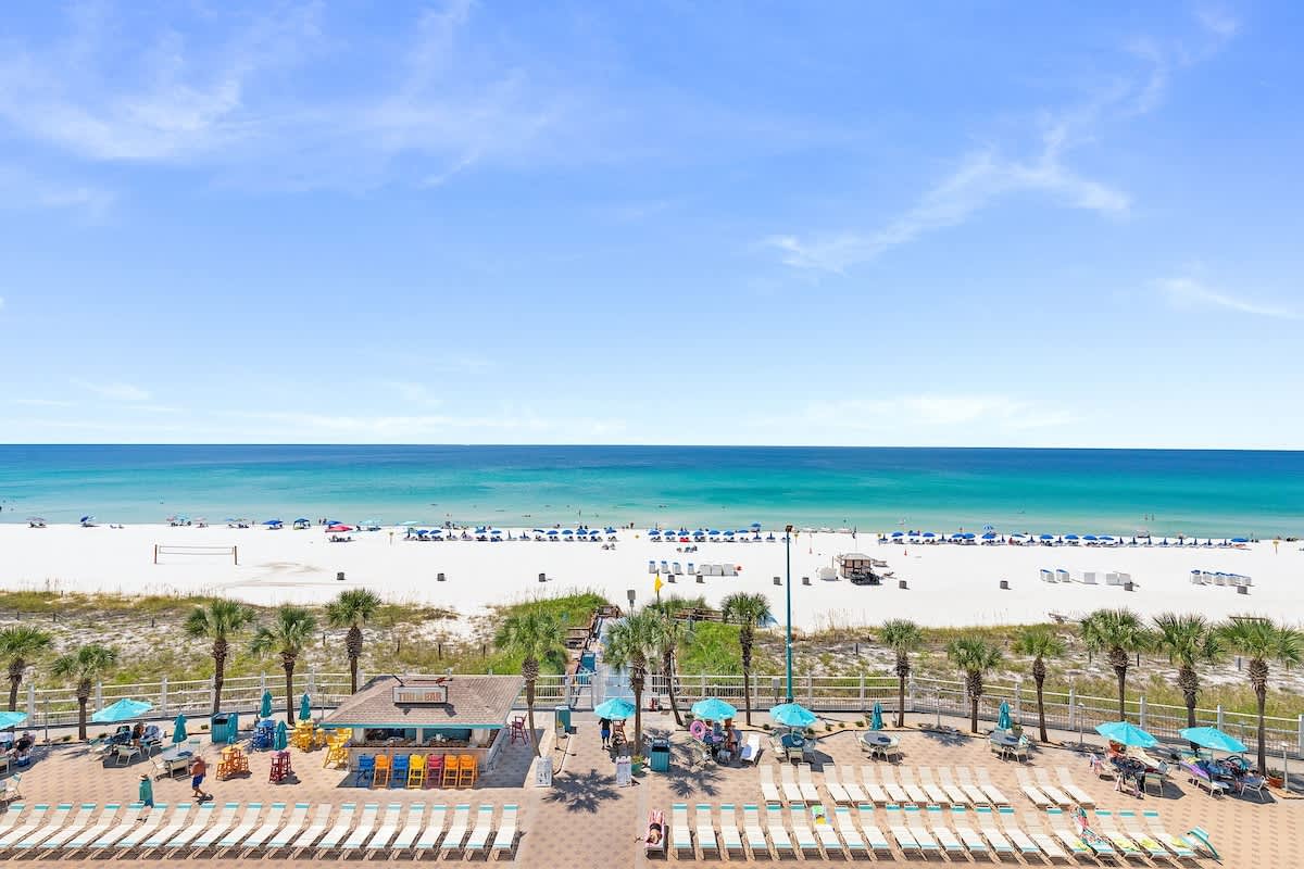 The Summit 616 – Ocean view from balcony, pool area with lounge chairs, sandy beach with umbrellas in the distance.