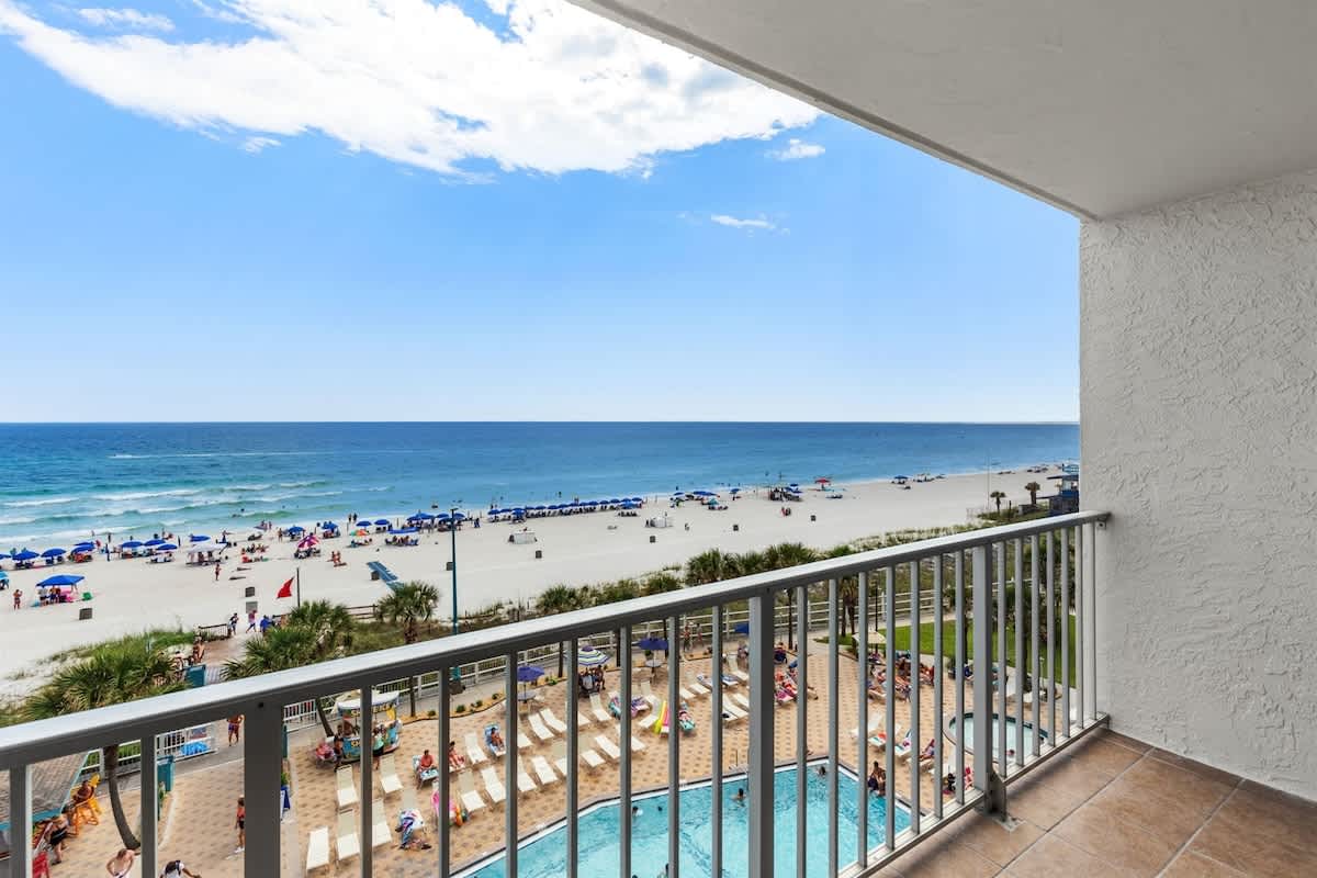 The Summit 616 – Balcony view of beach, ocean, and swimming pool with sun loungers below.