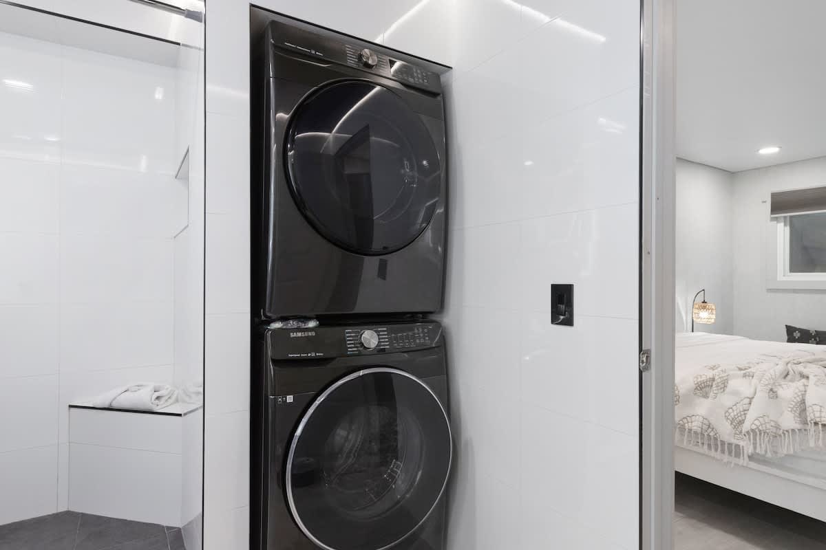 The Summit 616 – Washer and dryer unit next to a glass shower, with a bedroom visible in the background.