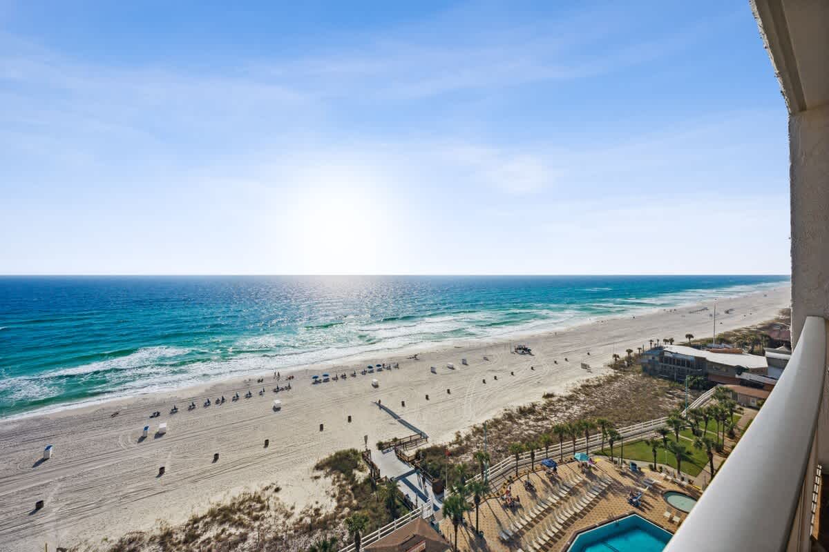 The Summit 1322 – Ocean view from a balcony overlooking the beach, with a pool and palm trees visible below.