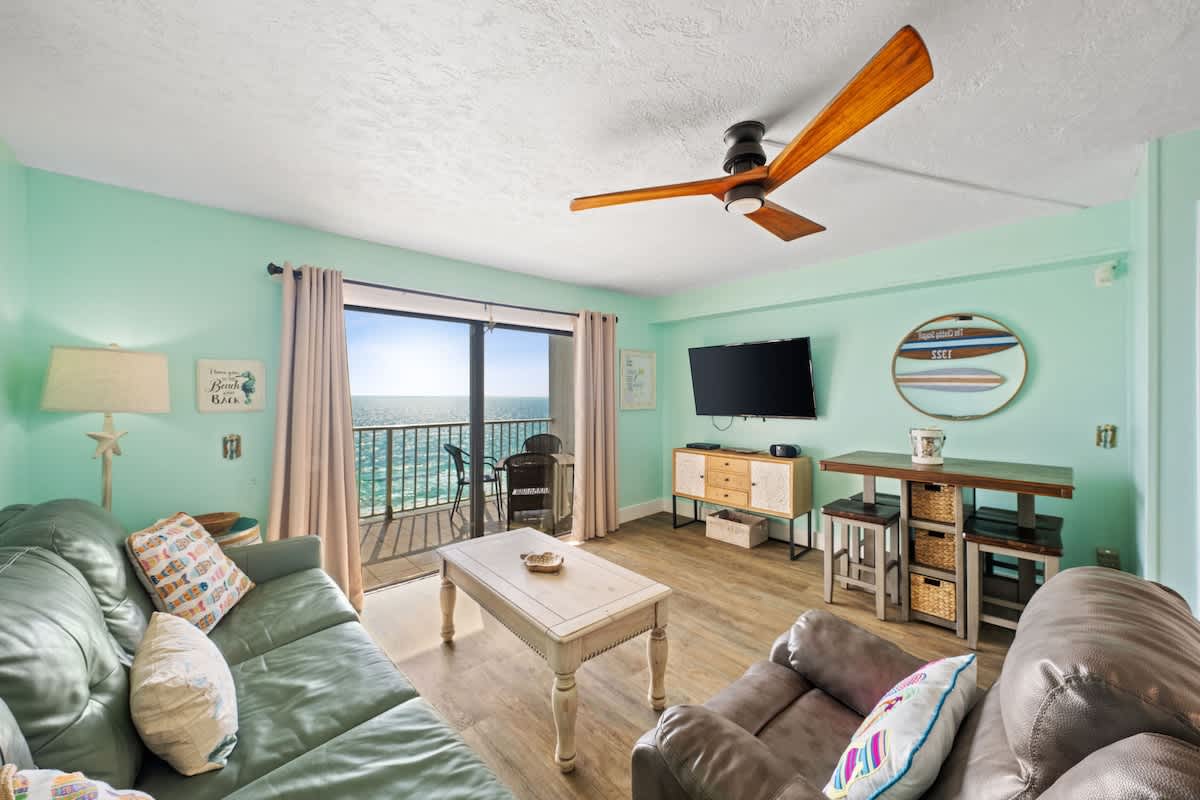 The Summit 1322 – Living room with teal walls, ocean view balcony, couch, and wooden coffee table.