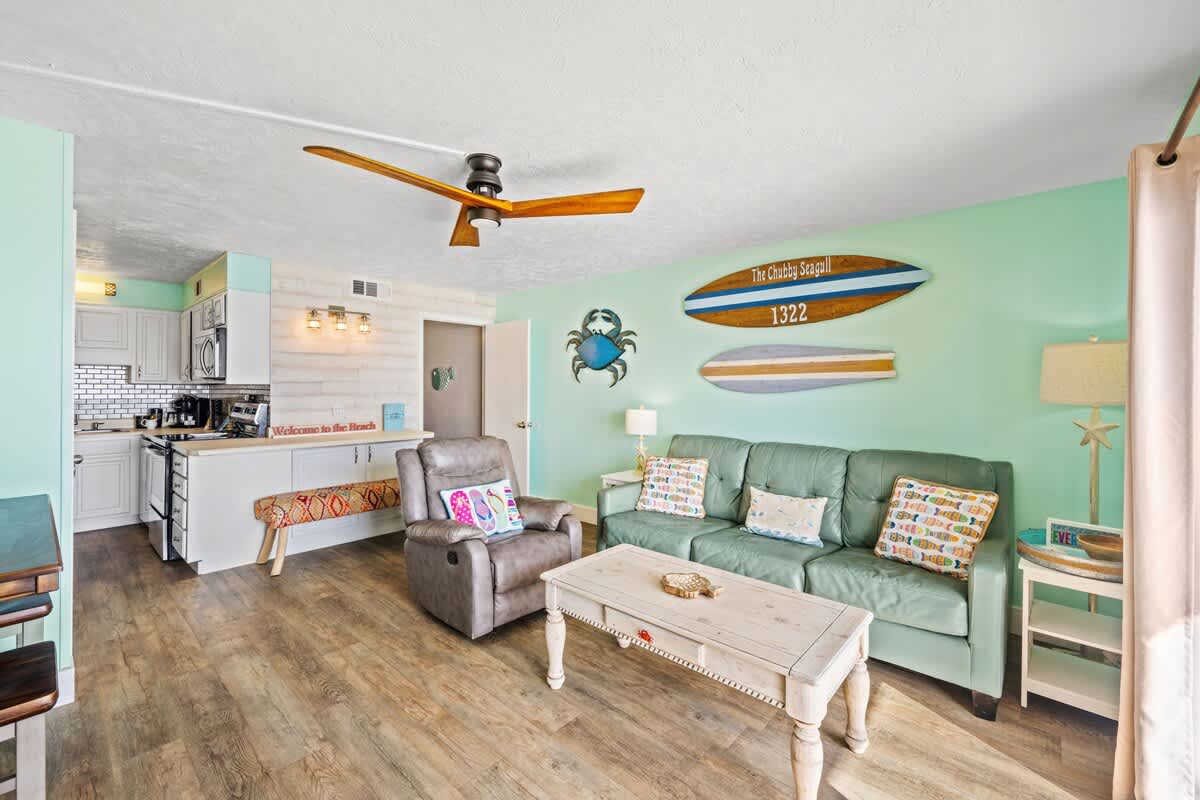 The Summit 1322 – Living room with light green walls, a sofa, coffee table, and decorated with surfboards and coastal decor.