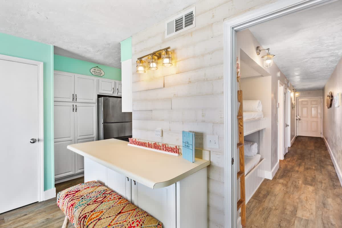 The Summit 1322 – Bright kitchen with a bar, white cabinets, and hallway leading to bedrooms.
