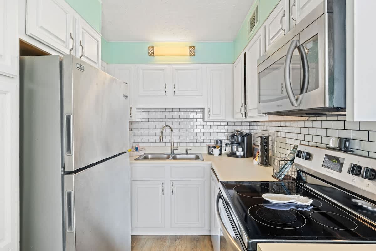The Summit 1322 – Bright kitchen with stainless steel appliances, white cabinets, and a tile backsplash.