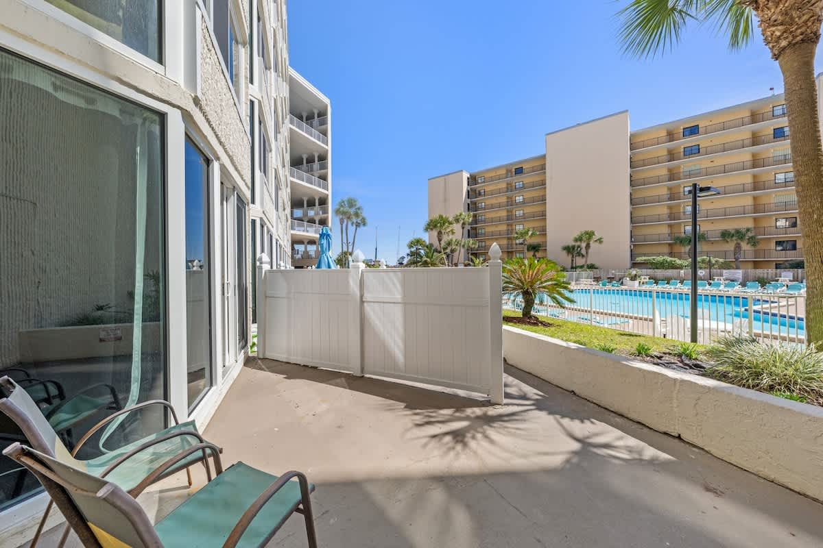 Top Of The Gulf 111 – Ground-level patio with two chairs and view of the pool area and surrounding buildings.
