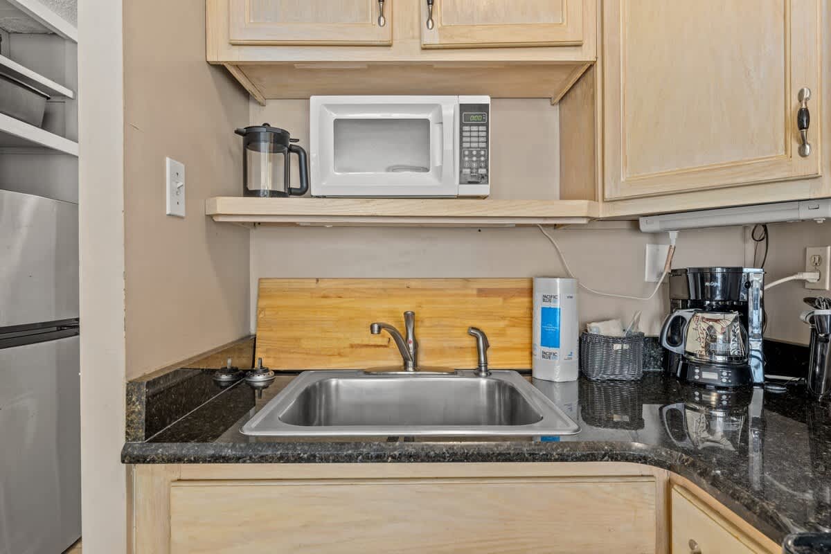 Top Of The Gulf 111 – Kitchen area with stainless sink, microwave, and coffee maker, featuring wooden countertops and dark granite surfaces.