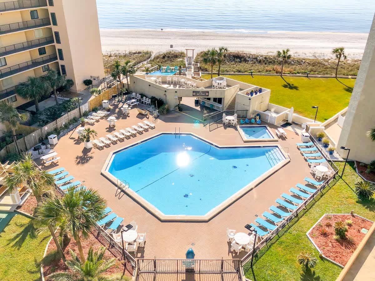 Top Of The Gulf 111 – Overview of a pool area with sun loungers and tropical landscaping, ocean visible in the background.